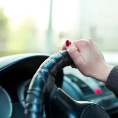 Dłoń kobiety na kierownicy, zastanawia się, ile kosztuje egzamin na prawo jazdy.