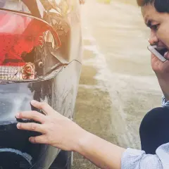 Zniszczony zderzak i lampa po kolizji. Mężczyzna zdenerwowany rozmawia przez telefon, prawdopodobnie wzywając pomoc lub zgłaszając zdarzenie, które może skutkować mandatem za spowodowanie kolizji.