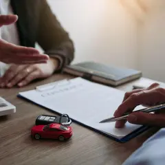 Podpisanie umowy leasingowej. Na stole leżą kluczyki do auta, czerwony samochodzik i kalkulator.
