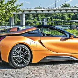 Pomarańczowy BMW i8 Roadster na bruku, pod mostem. Sprawdź aktualną bmw i8 cena.