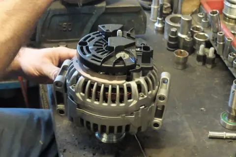 Warsztat samochodowy. Mechanik pracuje nad regeneracją alternatora. Sprawdź, jaka jest regeneracja alternatora cena.