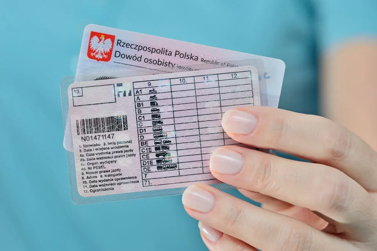 Dłoń trzyma polskie prawo jazdy kategorii B i dowód osobisty. Dokumenty są gotowe do podróży.