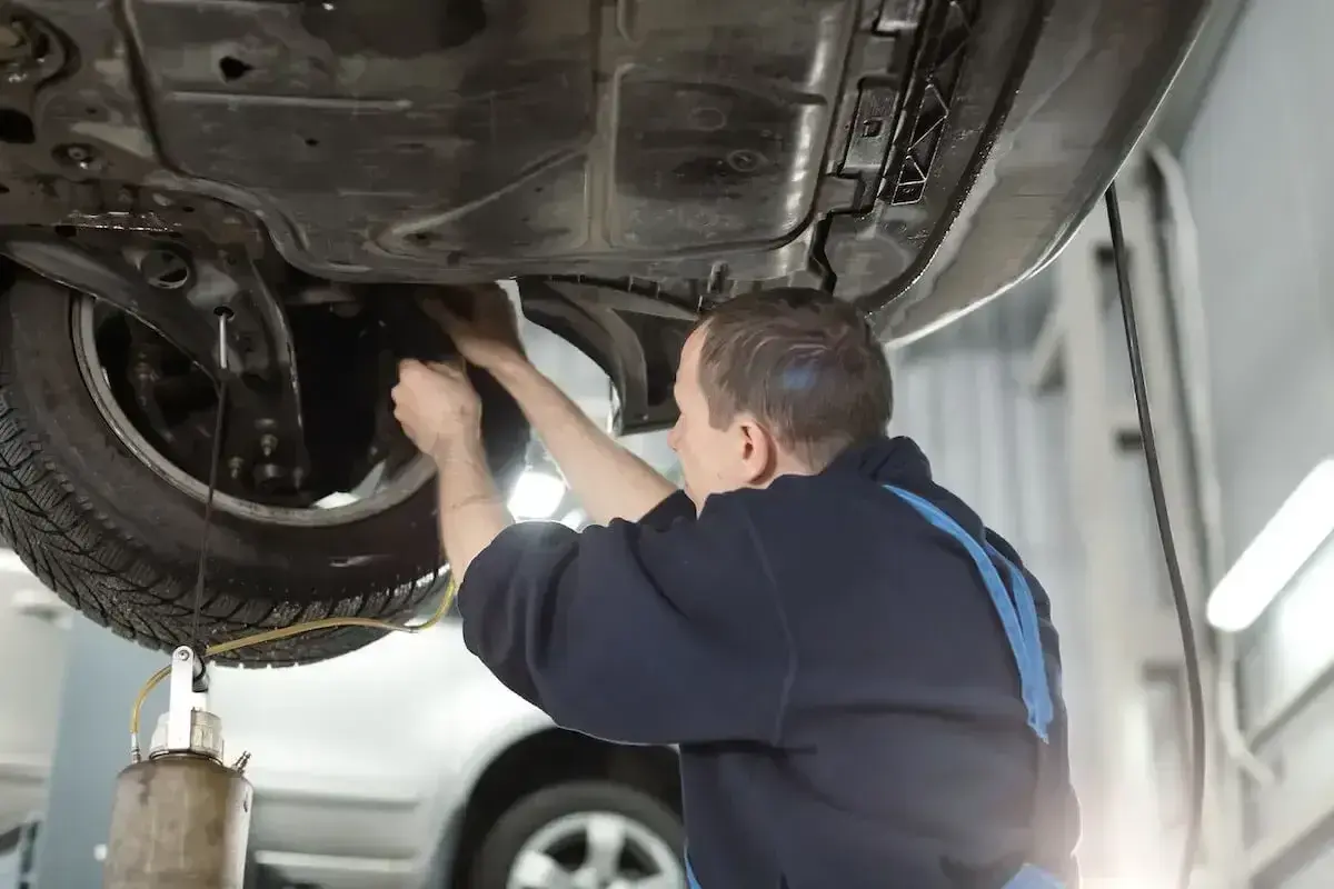 Mechanik wykonuje wymianę płynu hamulcowego w samochodzie podniesionym na podnośniku.