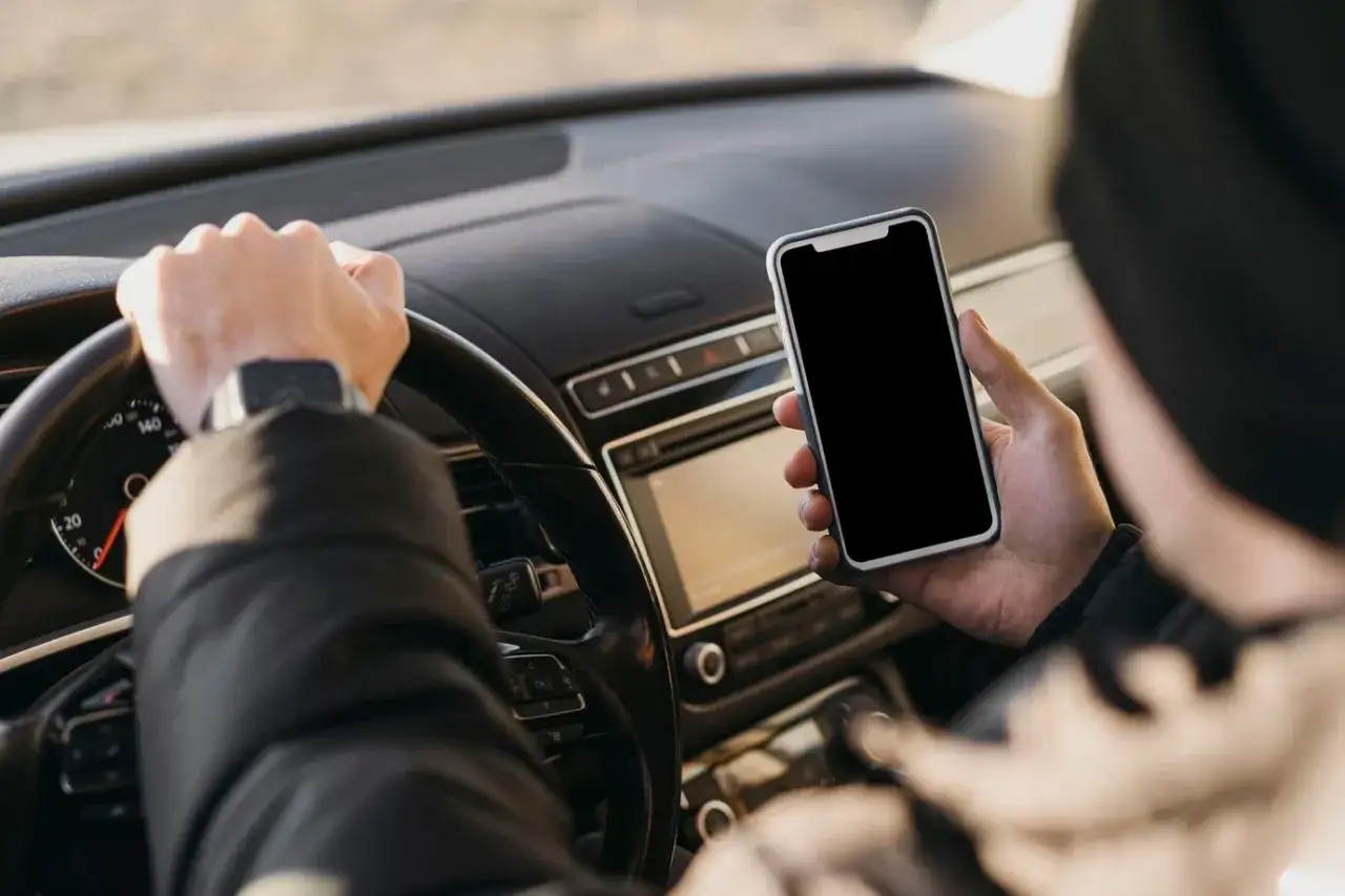 Kierowca trzyma telefon, zastanawiając się, ile punktów za telefon dostanie za takie zachowanie.