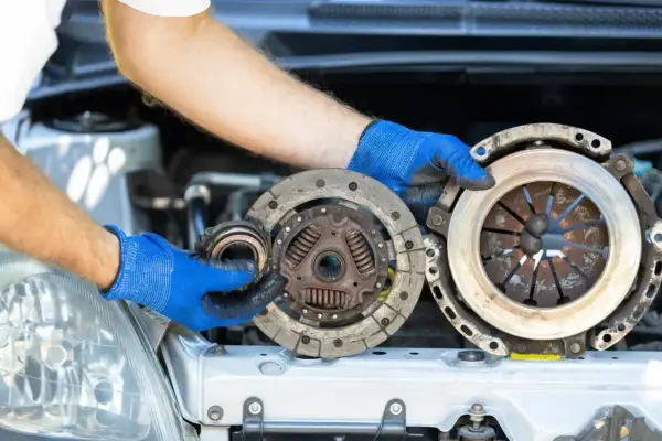 Mechanik w niebieskich rękawiczkach pokazuje zużyte części sprzęgła. Poznaj wymiana sprzęgła koszt i dowiedz się, kiedy warto je wymienić.